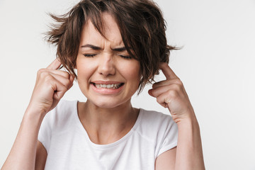 Pretty displeased stressed woman posing isolated over white wall background covering ears because of loud.