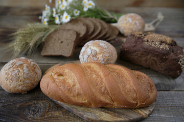 rye and wheat fresh hot bread with ears and a bouquet of daisies on a wooden rustic background, close-up