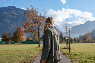 Fototapeta premium A young girl walks and dances in the city against the backdrop of the mountains. Beautiful autumn landscape in Interlaken, Switzerland. Beauty of fall nature. Happy woman on travel. Tourist lifestyle