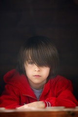 Preteen boy in red sweatshirt, hiding behind a wooden door, looking scared