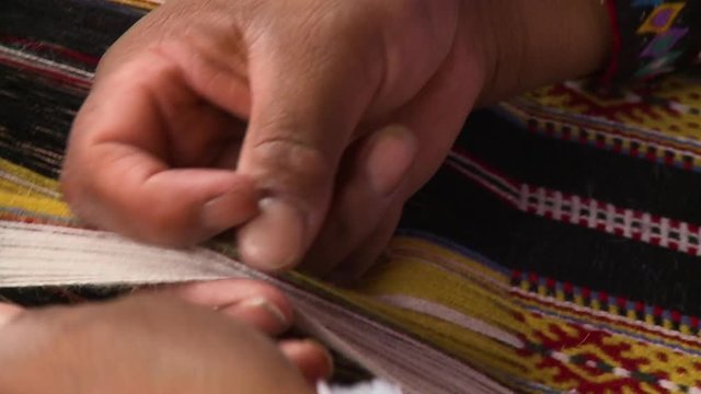 Extreme close-up high-angle panning shot of an indigenous Peruvian woman  on a colourful traditional jacket decorated with white buttons,  weaving  using a handloom, Andes, Peru