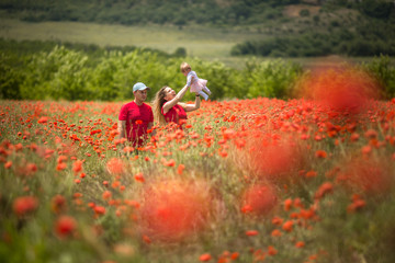 Happy family in a red poppy flower field. Mom and newborn girl laugh and rejoice. Mom holds her beloved daughter in her arms.