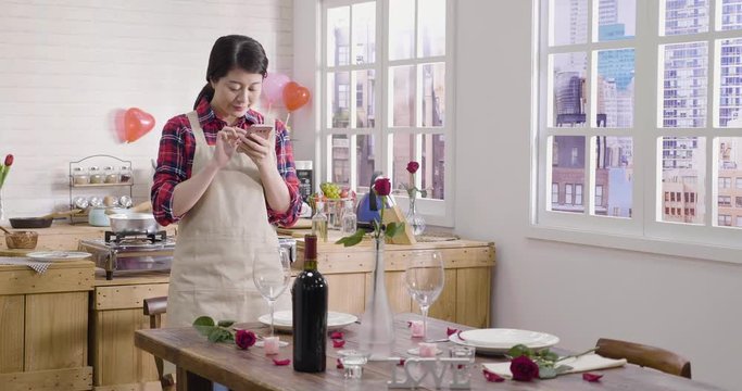 elegant housewife prepared ready for valentine's day romantic dinner at home. young woman taking picture of beautiful dining decorated table with flowers roses. female send photo to lover smile wait