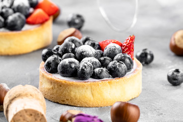 Blueberry and strawberry shortcake. There are hazelnuts, roses and wine corks on the table. Stone background.