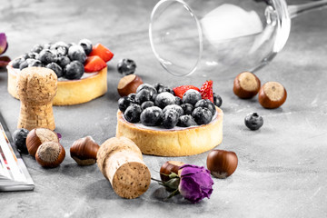 Blueberry and strawberry shortcake. There are hazelnuts, roses and wine corks on the table. Stone background.