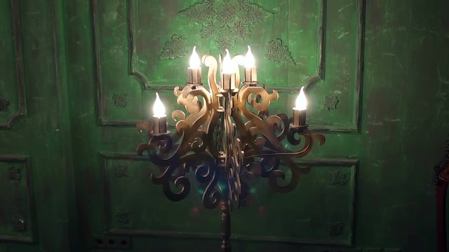 Old vintage chandelier with lamps in the shape of candles against the background of green vintage old wall. Dark backgro