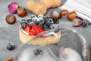 Blueberry and strawberry shortcake. There are hazelnuts, roses and wine corks on the table. Stone background.