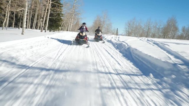 Action shot showing happy family driving skimobiles in the forest road. Panning shot as couple with their children are racing on the forest road.