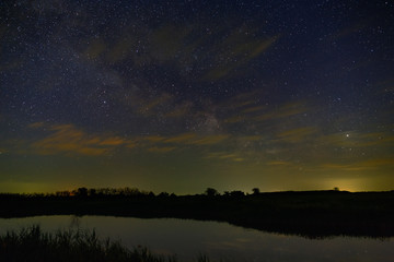 Bright stars with clouds over the river in the night sky. Outer space photographed with long exposure.