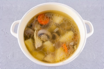 Bowl of chicken broth with champignons mushrooms close-up on gray background