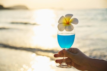 Closeup woman hand holding cocktail glass decoration with plumeria flower with beach background - happy relax celebration vacation in sea nature concept