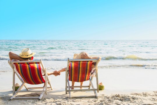 Relax couple lay down on beach chiar with sea wave background - man and woman have vacation at sea nature concept