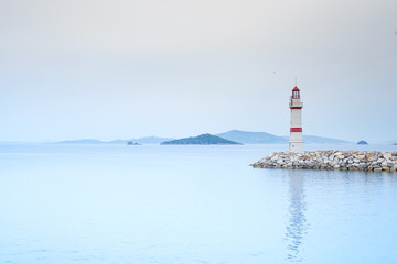 Lonely lighthouse on a stone road in the middle of the sea with views of the mountains and fog