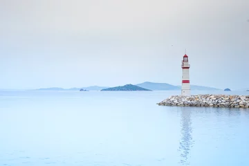 Foto auf Acrylglas Lonely lighthouse on a stone road in the middle of the sea with views of the mountains and fog © YuliiaMazurkevych
