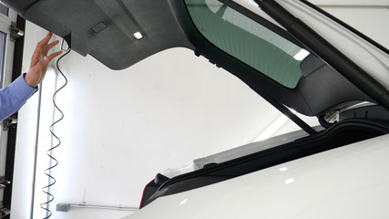 A young portrait guy in a shirt and shorts at an autocenter (service) opens (closes) the trunk while pressing a button. Concept of: New car, Salon, Quality, Slow shooting.