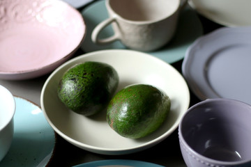 Collection of pottery and kitchenware in muted pastel colors with two avocados. Selective focus.