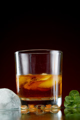 Glass with alcohol in a transparent glass with ice and mint on a red background