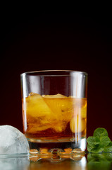 Glass with alcohol in a transparent glass with ice and mint on a red background