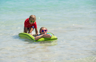 Sister and brother have fun with air mattress at the beach. Happy children during summer vacations.