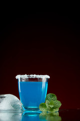 Glass with original alcoholic drink with mint and ice on red background