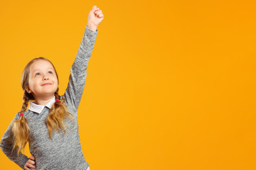 Closeup portrait of a little girl on a yellow background. The child raised his hand up. The concept...