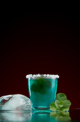Glass with original alcoholic drink with mint and ice on red background