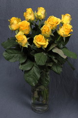 A large bouquet of yellow roses in a glass vase. On a gray background.