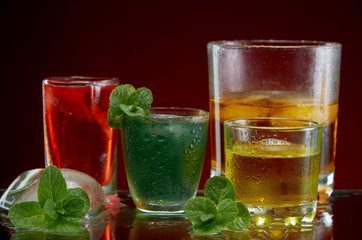 Three different alcoholic drinks in clear glasses with ice and mint on red background