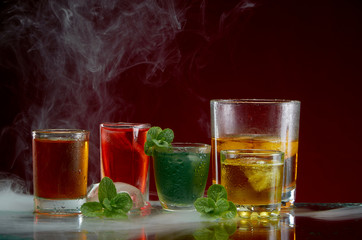 Alcoholic drink with ice and mint in a light smoke on the red background