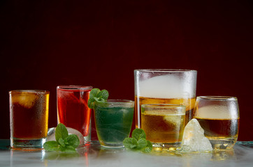 Different alcoholic cocktails with ice and mint with light smoke on a red background