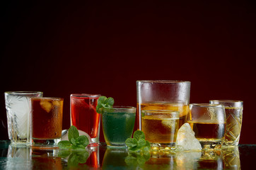 Color septet of alcoholic beverages in transparent glass glasses with ice and mint in smoke on a red background