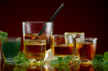 Various alcoholic cocktails in clear glasses with ice and mint on a red background