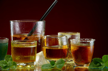 Various alcoholic cocktails in clear glasses with ice and mint on a red background