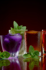 A wonderful set of alcoholic drinks in glasses with ice and mint on a red background