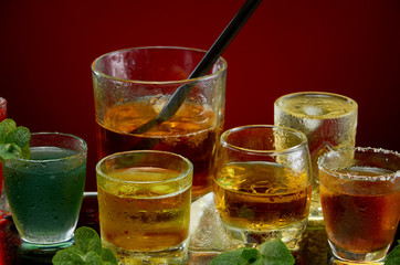 Glasses with various alcoholic drinks with ice and mint on red background