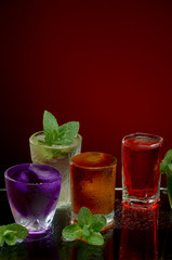 Colored alcoholic drinks with ice and mint on red background