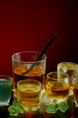 Colored alcoholic drinks with ice and mint on red background