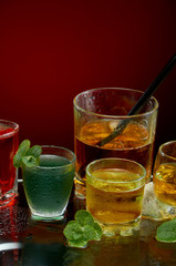 Colored alcoholic drinks with ice and mint on red background