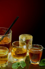 Colored alcoholic drinks with ice and mint on red background
