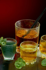 Colored alcoholic drinks with ice and mint on red background