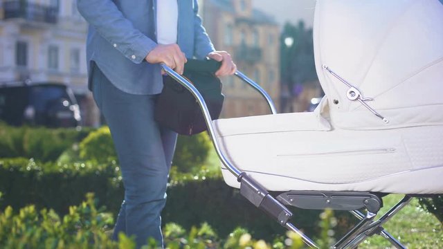 Young man pushing baby pram walking in park, taking care of infant, parenthood