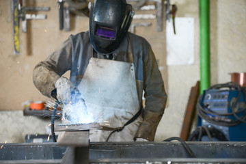 handsome man workshop welding iron spark fire hot steel with power GMAW welder and protective gear