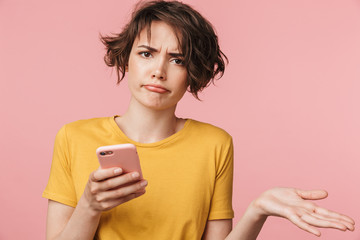 Confused young beautiful woman posing isolated over pink wall background using mobile phone.