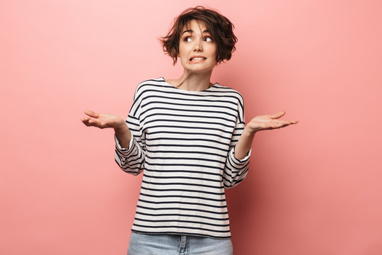 Confused unsure beautiful woman posing isolated over pink wall background.