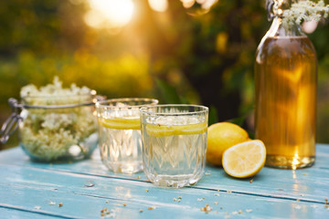 Elderflower lemonade with bottle of syrup and elderberry flowers at sunset