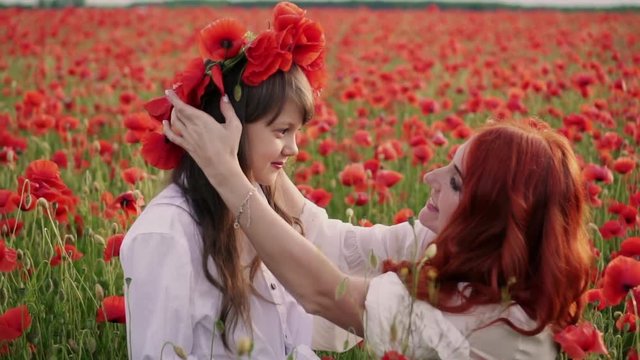 Young mother puts wreath of poppy flowers on her daughter's head, slow motion