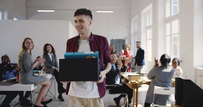 Happy young Caucasian male office employee walks into new multiethnic office hired on a new job, colleagues welcome him.