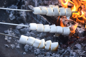 Three skewers of marshmallows toasting on a fire