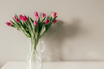 Glass vase with bouquet of beautiful tulips on grey wall background.