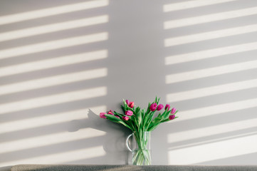 Glass vase with bouquet of beautiful tulips on grey wall background.